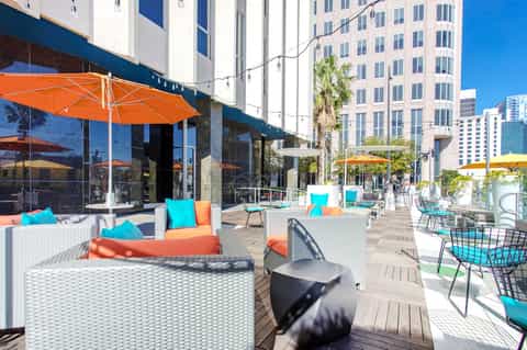 Outdoor rooftop lounge with white furniture, orange umbrellas, and city skyline views framed by tall buildings