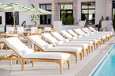 Poolside lounge area with rows of wooden sunbeds, white cushions, and striped umbrellas
