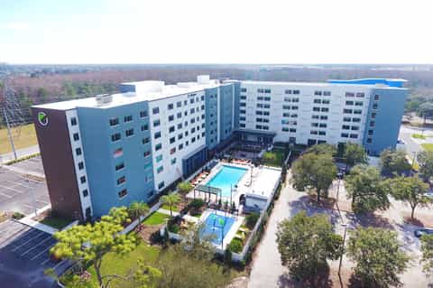 Aerial view of modern blue and white apartment complex with central pool and courtyard surrounded by landscaping