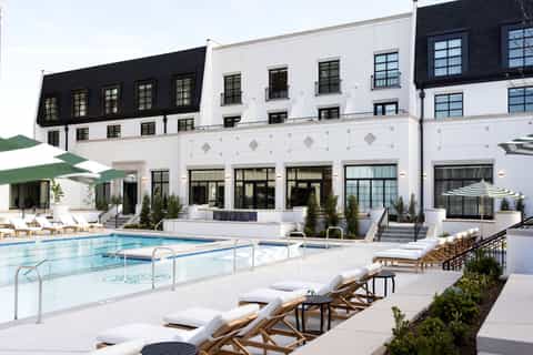 Modern hotel exterior with white facade, black mansard roofs, and lounge chairs by pool