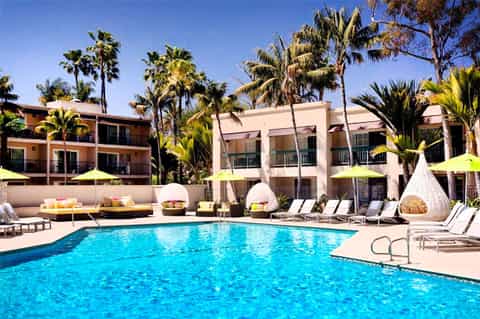 Resort pool with turquoise water surrounded by palm trees, lounge chairs, and colorful umbrellas
