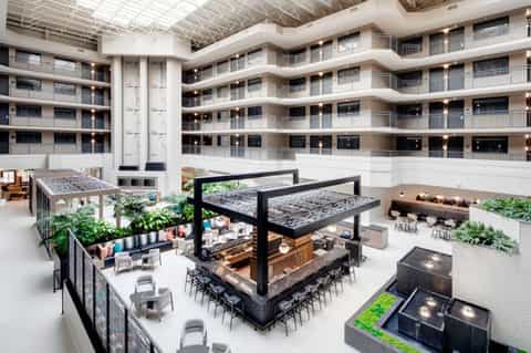 Multi-story hotel atrium with central bar, seating areas, plants, and skylighting