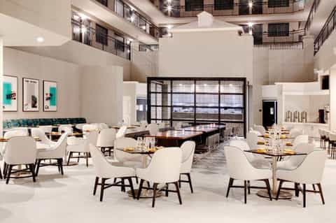 Modern restaurant dining area with white chairs, high ceilings, and large windows