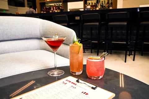 Cocktails on black table by gray sofa in modern hotel bar with menu and dark bar seating