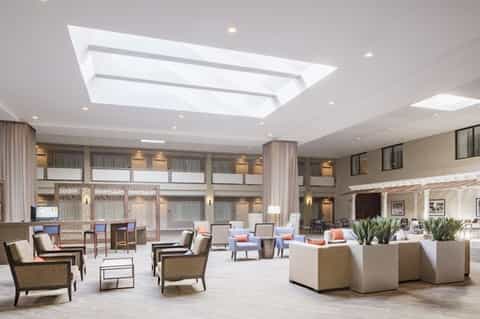 Spacious modern hotel lobby with skylight, seating areas, neutral tones, and contemporary furniture