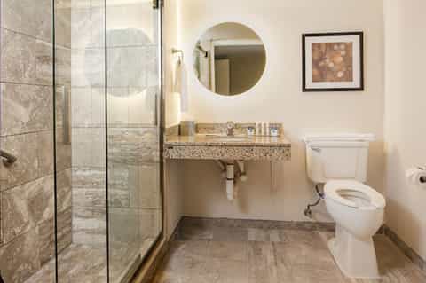 Modern bathroom with glass shower enclosure, granite countertop, and round mirror