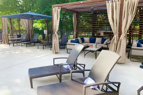 Outdoor patio with lounge chairs, pergola with curtains, sectional sofa, and lush green forest backdrop