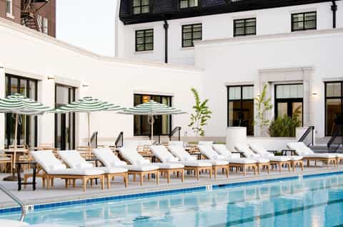 Luxury poolside resort with white loungers, striped umbrellas, and elegant white building facade
