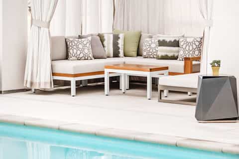 Luxury poolside lounge area with cream seating, decorative pillows, and sheer curtains by turquoise water