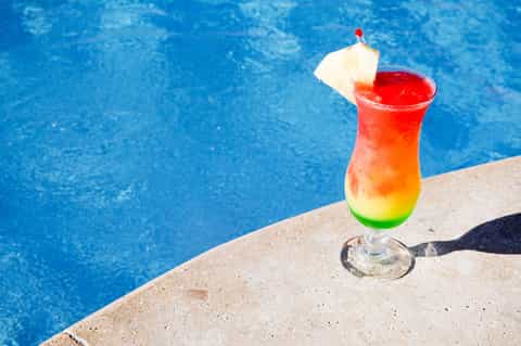 Colorful tropical cocktail with pineapple garnish by a bright blue swimming pool