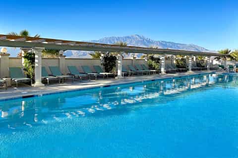 Resort pool with turquoise water, lounge chairs under pergola, and mountain views in background