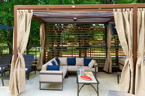 Modern pergola with cream curtains sheltering sectional sofa and coffee table on patio