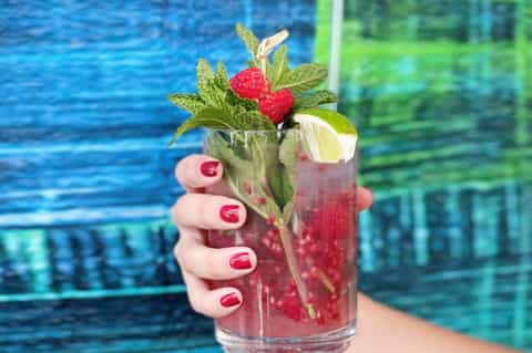 Tropical cocktail with raspberries and mint garnish by a swimming pool