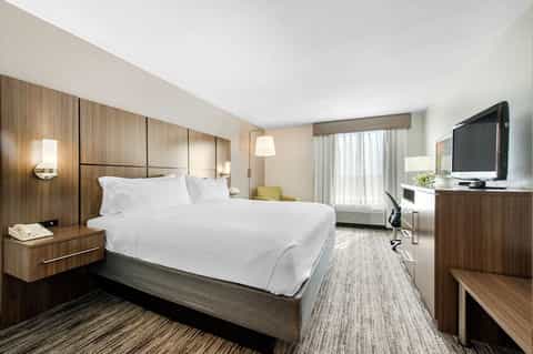 Modern hotel bedroom with wood headboard, white linens, TV, and natural light