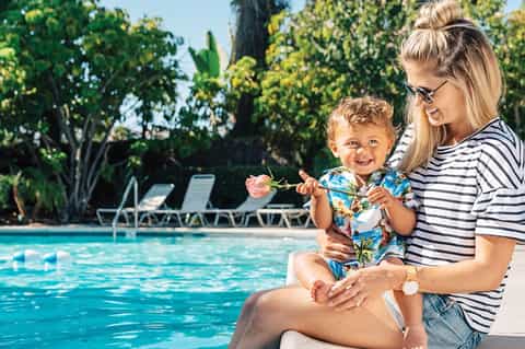Woman and toddler by resort pool playing with toys on sunny day