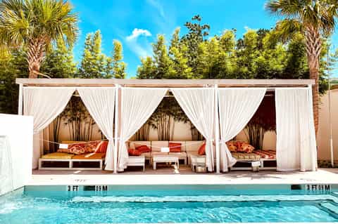 Luxury poolside cabanas with white curtains, cushioned beds, and turquoise pool