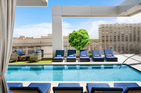Rooftop pool deck with blue loungers, modern pergola, city skyline, and lounge seating