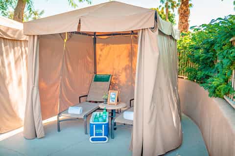 Private spa cabana with beige curtains, lounge chairs, and amenities in garden setting