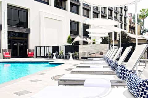 Modern resort pool deck with blue water, white lounge chairs, umbrellas, and contemporary building