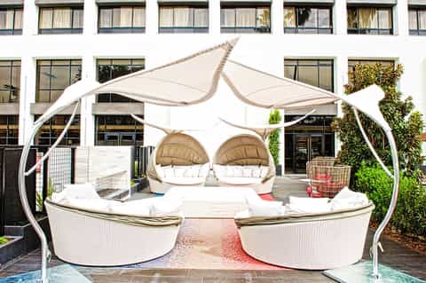Contemporary outdoor lounge area with white pod chairs under curved canopy and brick building