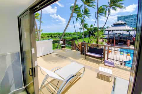 Beachfront balcony with lounge chairs overlooking pool, gazebo, and palm trees