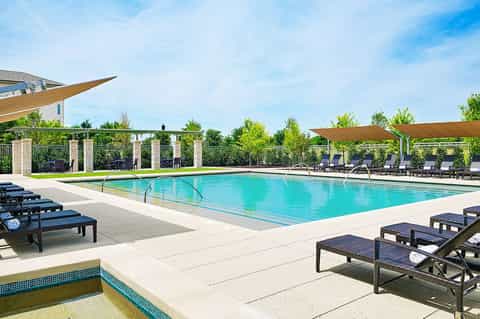 Olympic-size swimming pool with sun loungers, wooden pergola structures, and manicured landscaping