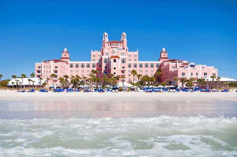 Historic pink beachfront hotel with towers and palm trees on sandy beach with ocean waves