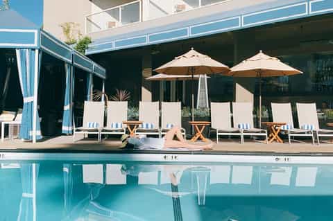 Woman relaxing poolside on lounge chair with umbrellas and cabanas reflected in clear water