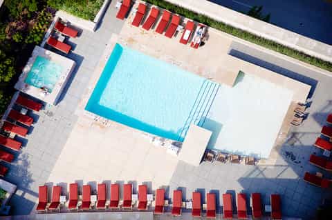 Aerial view of resort pool with turquoise water, red lounge chairs, and surrounding patio deck