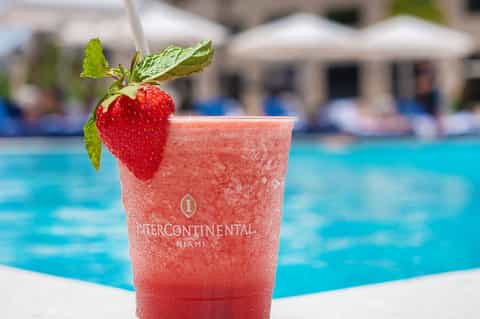 Strawberry-garnished cocktail with InterContinental Miami branding poolside with blue water background