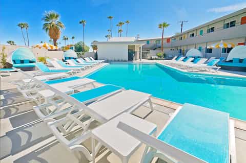Turquoise swimming pool with white lounge chairs and blue cabanas surrounded by palm trees