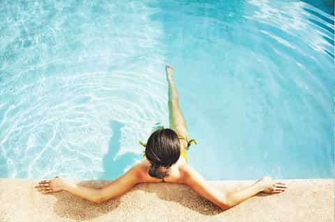 Person relaxing at edge of turquoise swimming pool with arms outstretched