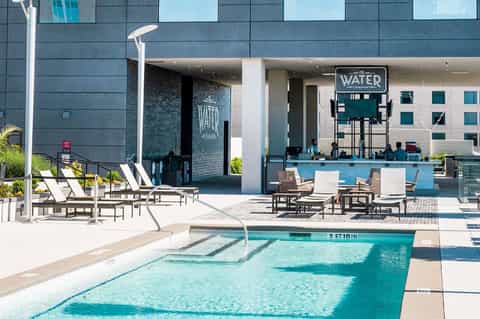Resort pool deck with turquoise water, lounge chairs, bar area, and modern building facade