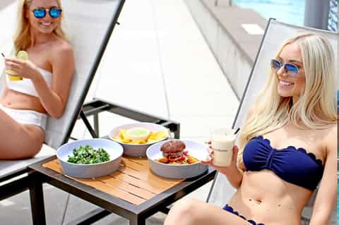 Woman in blue bikini enjoying healthy meal poolside with salad and beverage