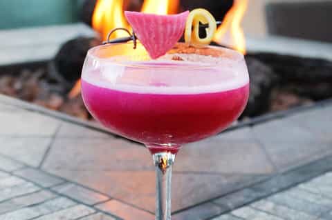 Pink cocktail with fruit garnish served by fire pit at dusk