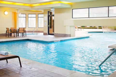 Indoor heated swimming pool with turquoise water and dining seating area with yellow lighting