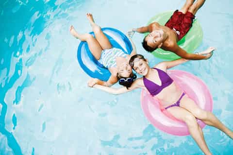 Family floating on colorful pool floats in clear turquoise water, overhead aerial view