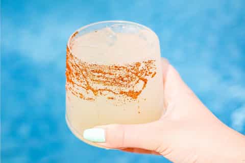 Frozen cocktail with cinnamon sugar rim held against bright blue poolside background