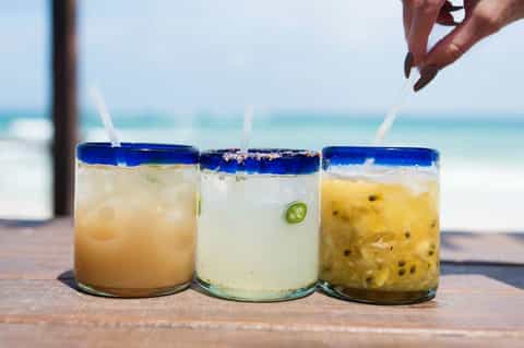 Three tropical cocktails with blue rim and straws on beach table
