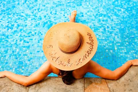 Woman in straw hat relaxing at pool edge with arms spread
