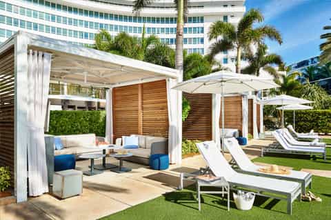 Luxury poolside cabanas with white pergolas, wooden privacy screens, lounge chairs, and manicured lawn