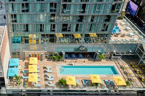 Aerial view of rooftop pool with yellow umbrellas, loungers, and multi-story building