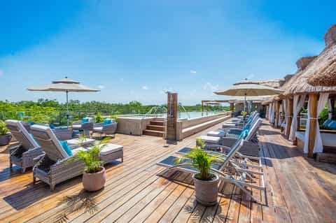 Waterfront resort deck with lounge chairs, umbrellas, and thatched-roof cabanas overlooking landscape