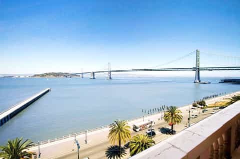 Bay Bridge spanning turquoise water with palm trees and beach in foreground under clear sky