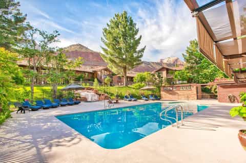 Resort pool with mountain views, blue loungers, pergola shade, and red rock formations