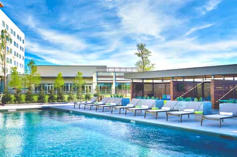 Modern resort pool with loungers, contemporary building, and clear blue sky