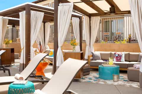 Upscale rooftop lounge with pergolas, white curtains, gray seating, and ocean horizon views
