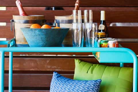 Turquoise metal console table with champagne bucket, glasses, fruit bowl, and decorative items against wooden wall backdrop