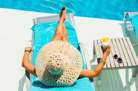 Overhead view of person in lounge chair by turquoise pool holding cocktail and sunglasses