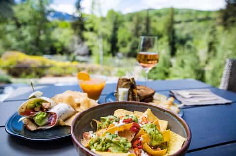 Outdoor dining table with tacos, guacamole, and beverages overlooking green mountains and valley